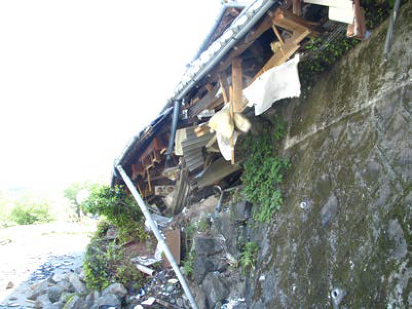 地震で被害を受けた崖の様子。崖とブロックが崩壊し、崖の上の家屋が崩れている。